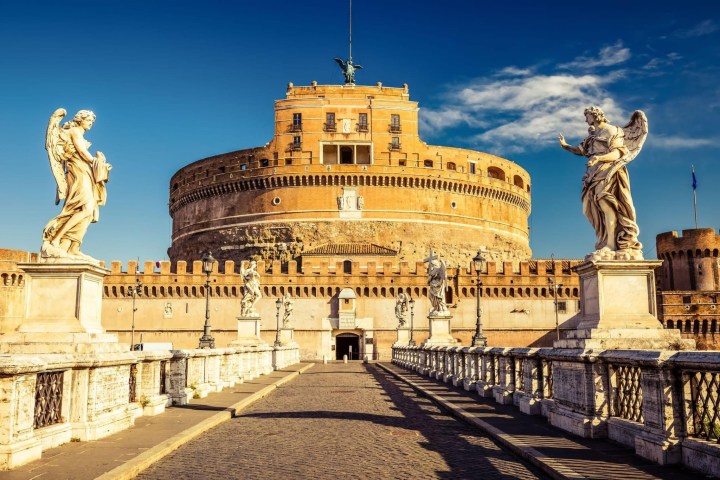 Stone castle with statues on bridge, clear sky in the background.