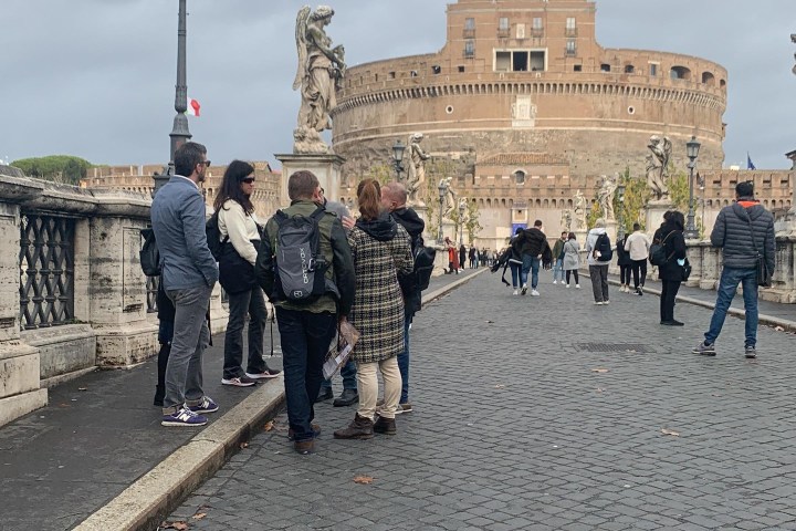 People standing on a cobblestone bridge with a historic castle in the background.