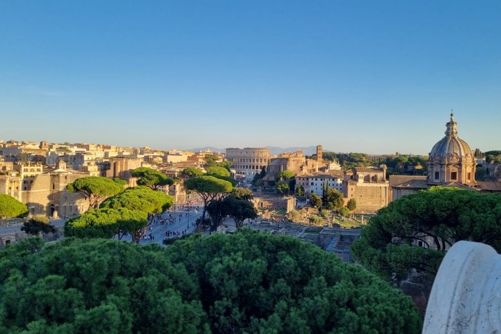 Panoramic view of ancient Roman architecture with dome and trees under a clear blue sky.