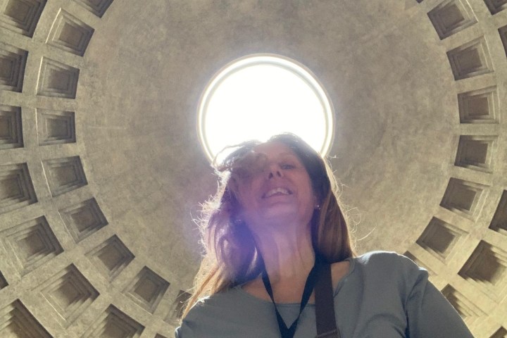 Person standing under circular dome with central skylight and geometric pattern.